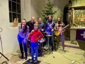 Eine Band mit Schlagzeug, Gitarre, Bass, Sängerin und Sänger steht im Chorraum der Neuender Kirche.